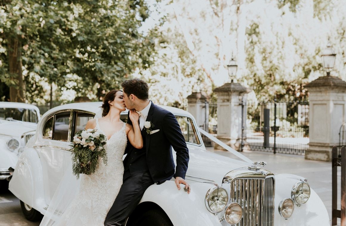 Bride and groom kissing beside vintage car